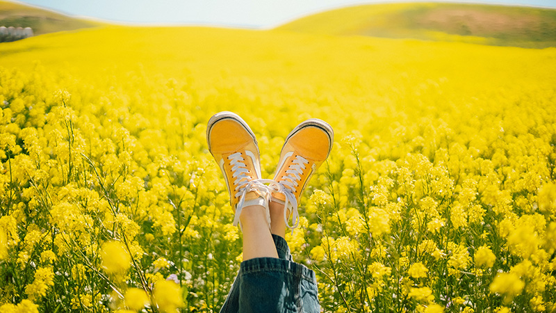 Ett par fötter med skor på, i närbild. I bakgrunden syns ett rapsfält.