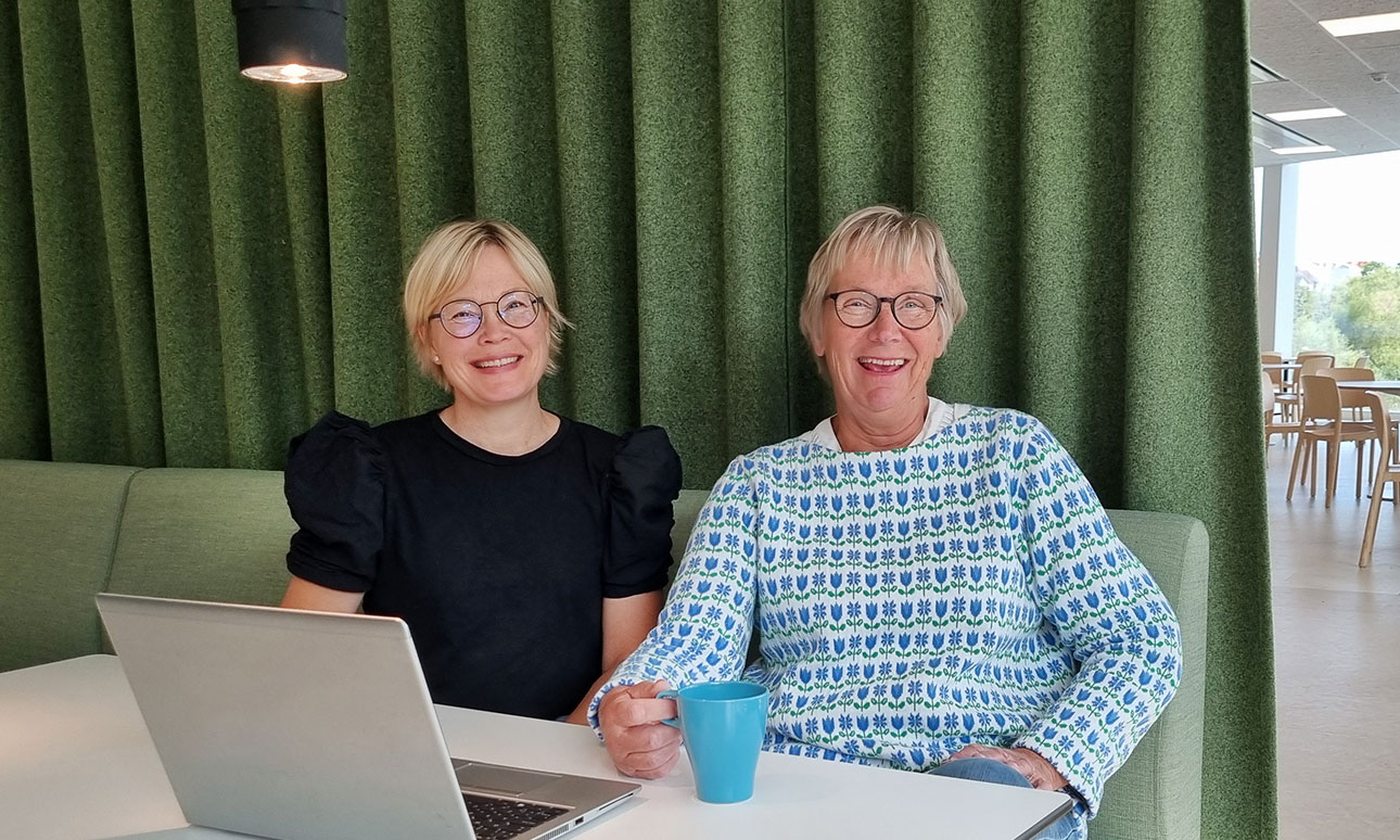 Anna Lundstedt och Eva Sundberg sitter vid en dator och har kaffemuggar i händerna