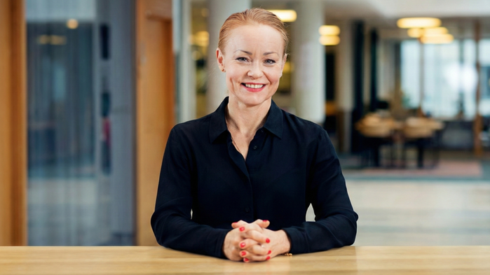 Kristine Wiklund sitter i ett kontorlandskap och har rött hår och svarta kläder