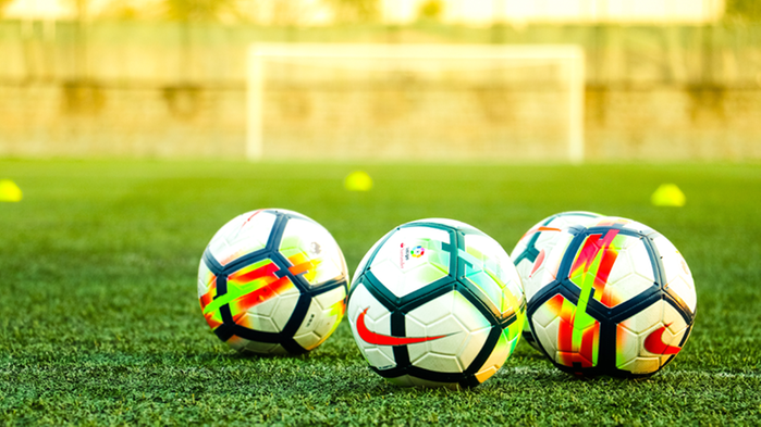 Fyra fotbollar ligger på en gräsplan med fotbollsmål i bakgrunden.