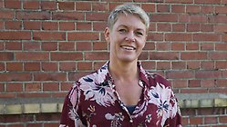 Jennie Cederholm Björklund har en blommig skjorta på sig och står framför en tegelbyggnad