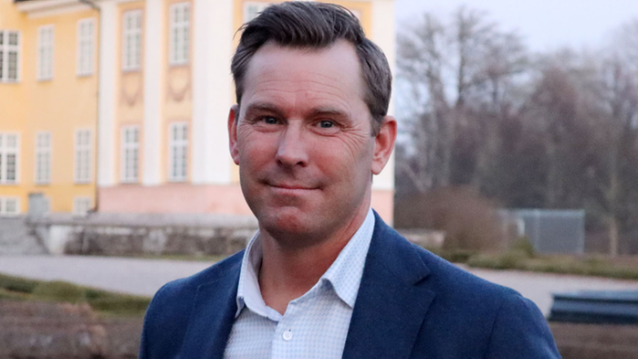 Johan Varenius som är verksamhetsledare på Agro Sörmland har ljusblå skjorta och mörkblå kavaj. Han står framför ett gult hus.