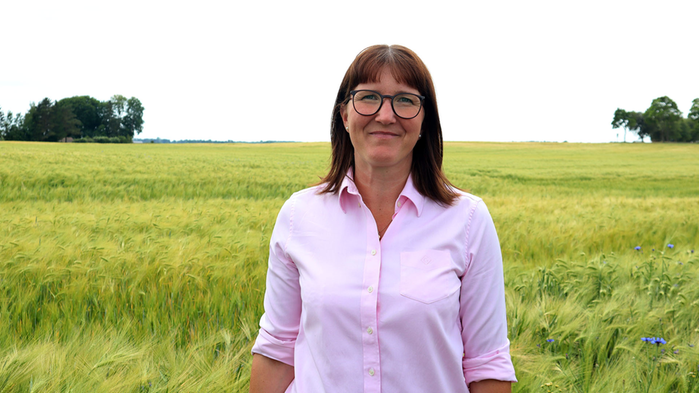 Karolina Muhrman har rosa skjorta på sig och står i ett sädesfält