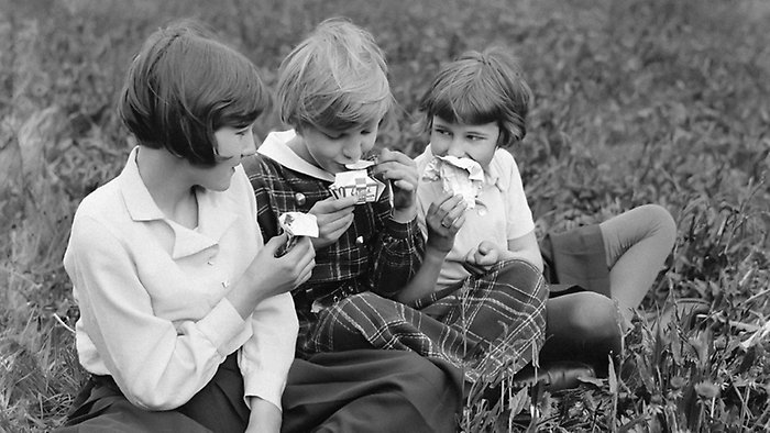 Gammalt foto med tre flickor som sitter i gräset och äter