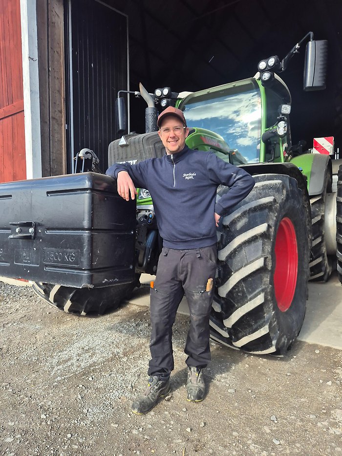 Joakim Vägermark står vid sin gröna traktor utomhus