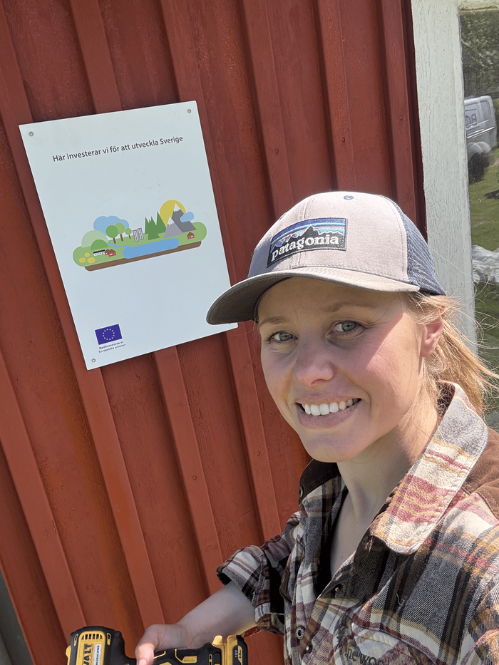 Johanna vid röd ladugårdsvägg med borr i handen
