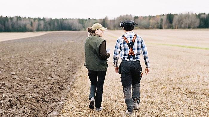 Två personer vandrar över ett plöjt fält. Man ser deras ryggtavlor.