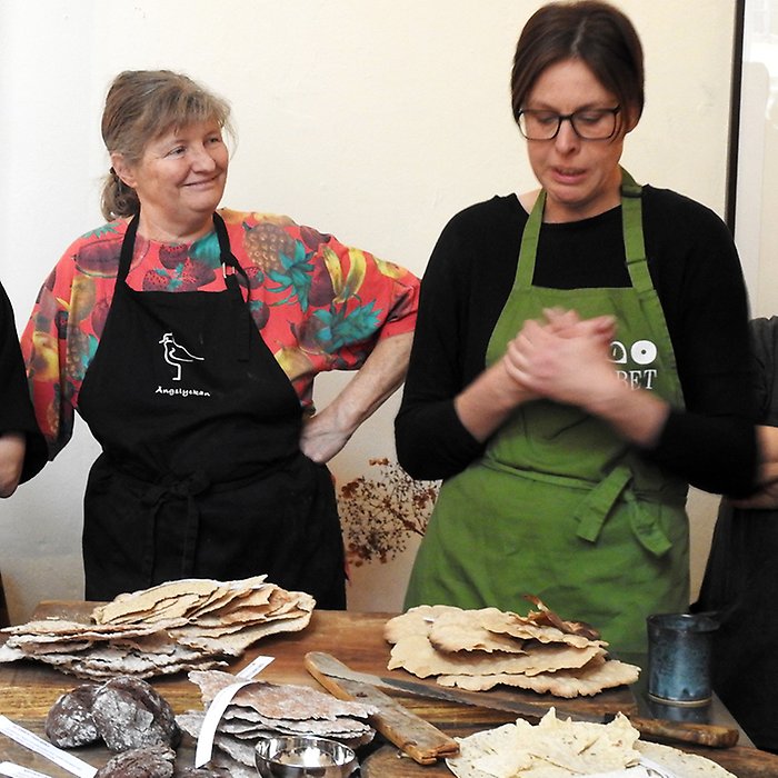 Två kvinnor vid ett bakbord. I förgrunden syns knäkebröd.