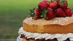 En sommartårta i närbild, den är gjort på sockerkaka och grädde och det är färska jordgubbar på toppen.